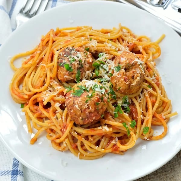 Spaghetti with meatballs, tomato sauce, grated cheese, and fresh parsley on a white plate.